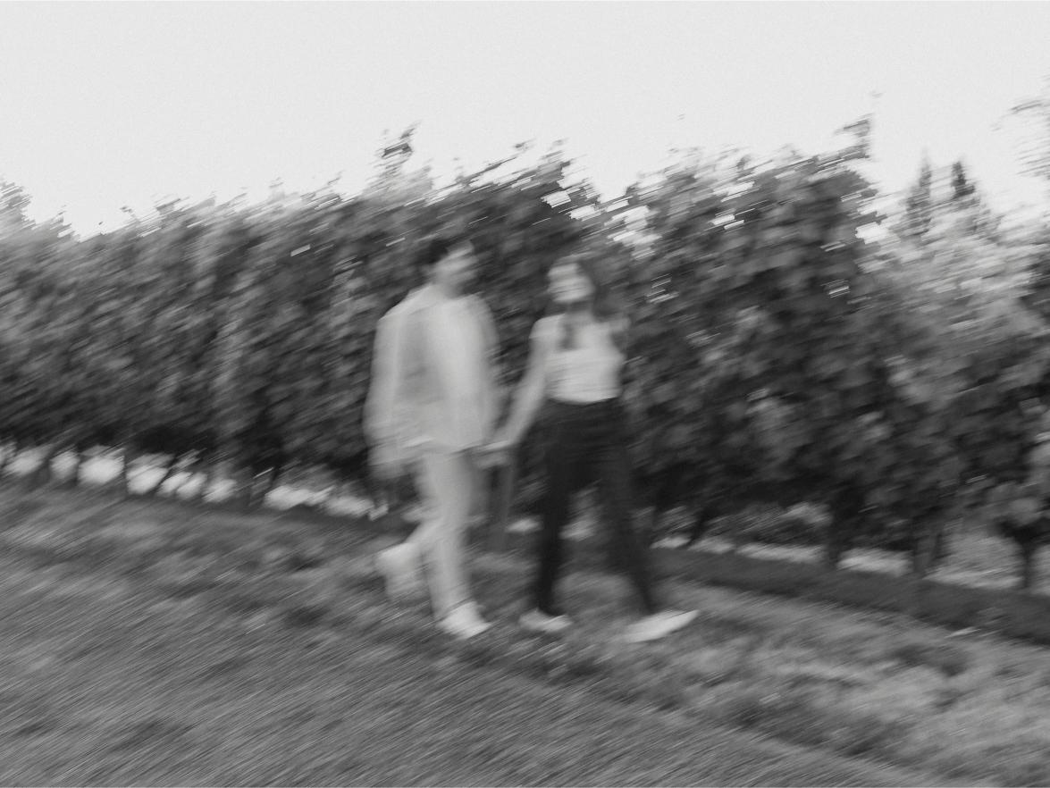 A blurry black and white photo of the couple walking through a vineyard